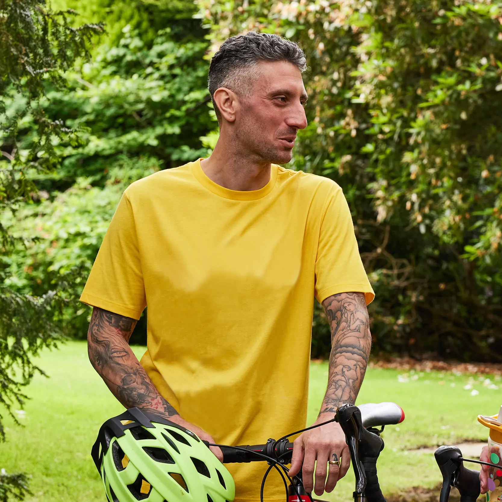 An adult smiling outside, bicycle in hand. 