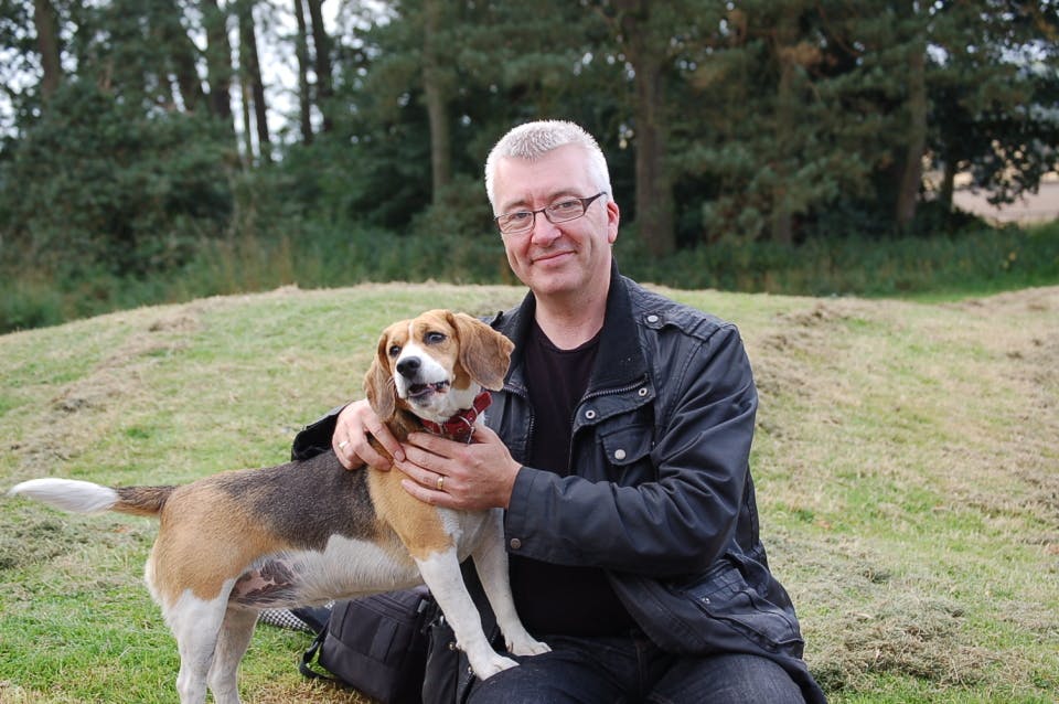 Peter sitting on grass outdoors with his beagle Clodagh, one arm around the dog.