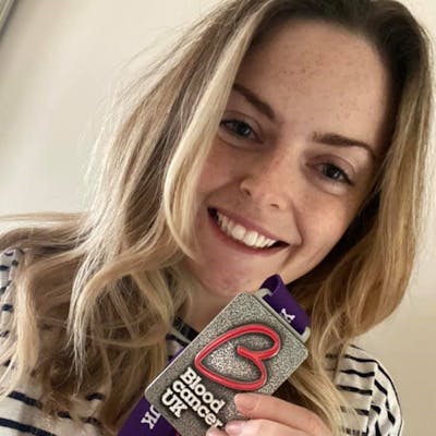 Photo of a Blood Cancer UK medal recipient smiling to camera whilst holding up her medal.