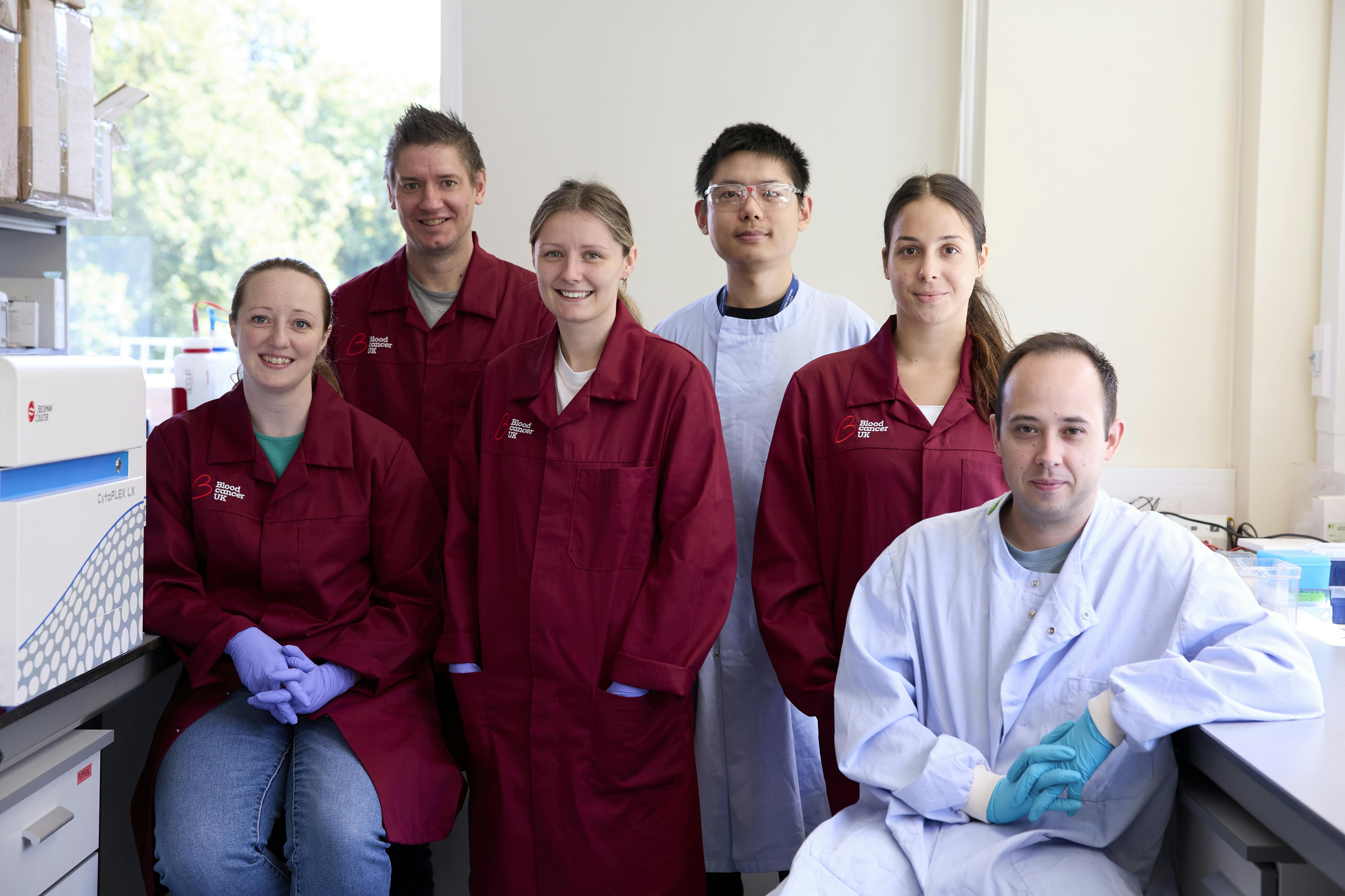 Photo of PhD students wearing white and burgundy lab coats smiling for the camera.