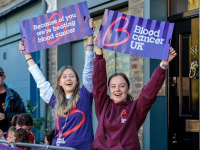 Photo of two Blood Cancer UK supporters holding BCUK signs behind a marathon barrier.