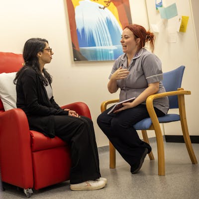 Clinical trial nurse and patient seated in a waiting room, chatting.