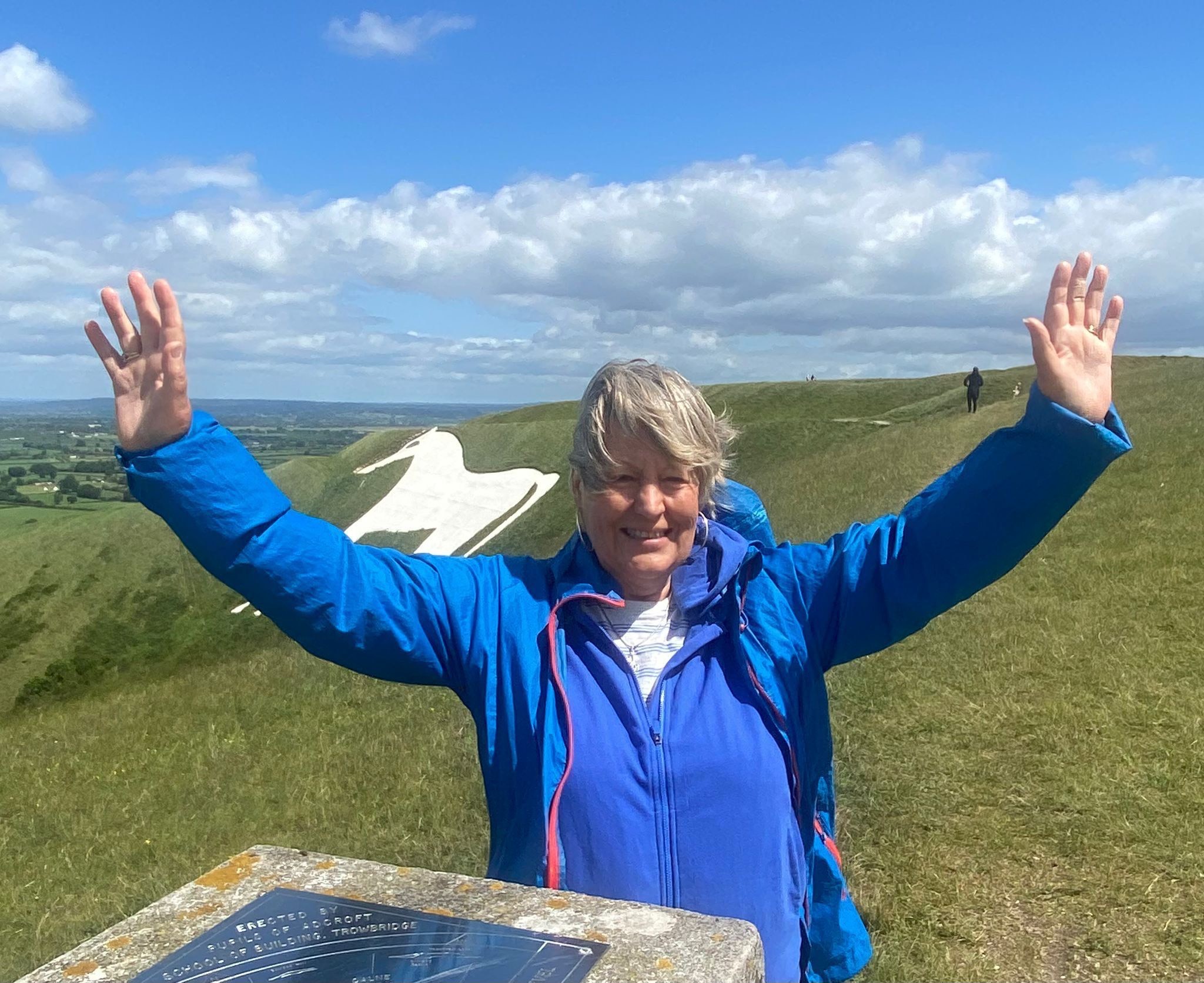 Jo smiling with arms outstretched atop a summit.