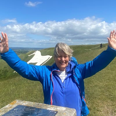 Jo smiling with arms outstretched atop a summit.