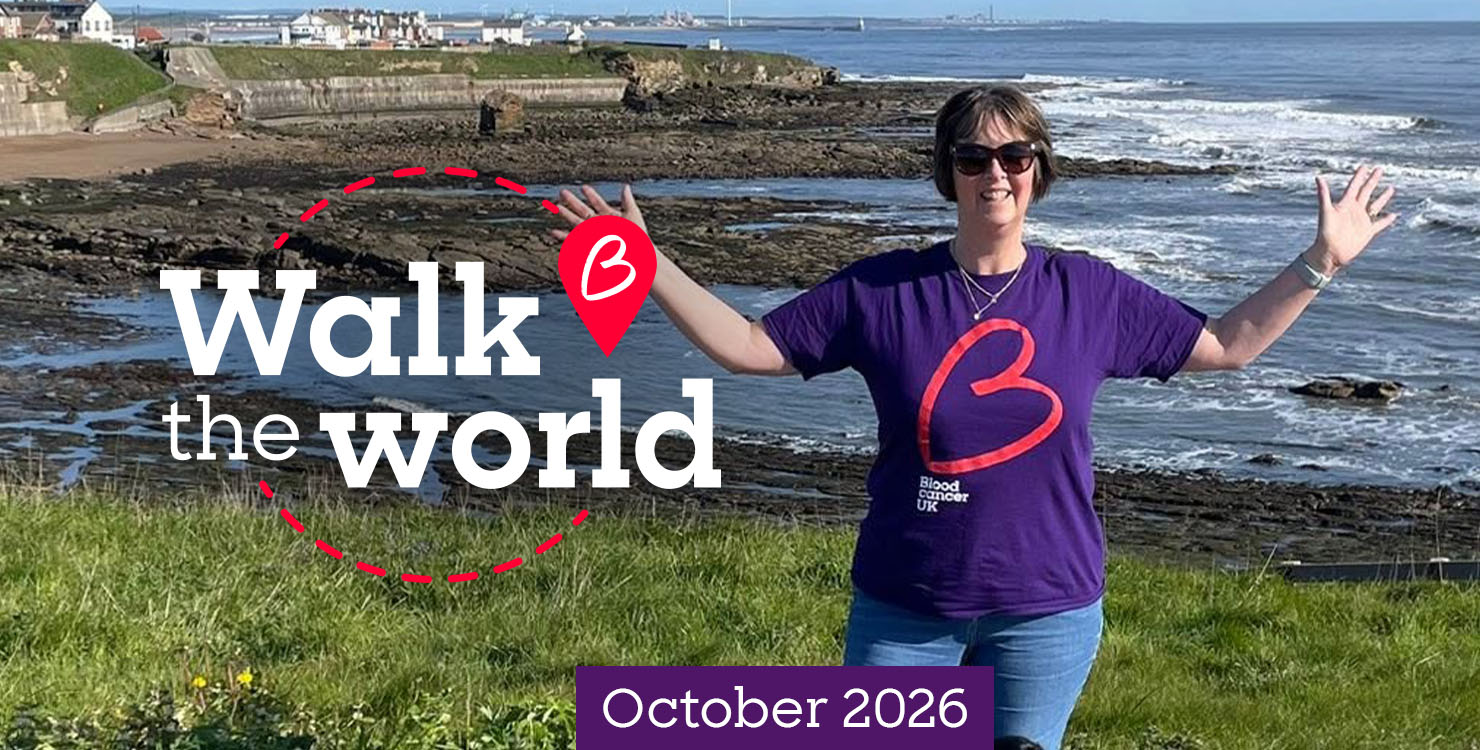 Person wearing a Blood Cancer UK t-shirt with arms outstretched, standing on a coastal cliff overlooking the sea for the Walk the World challenge, October 2026.