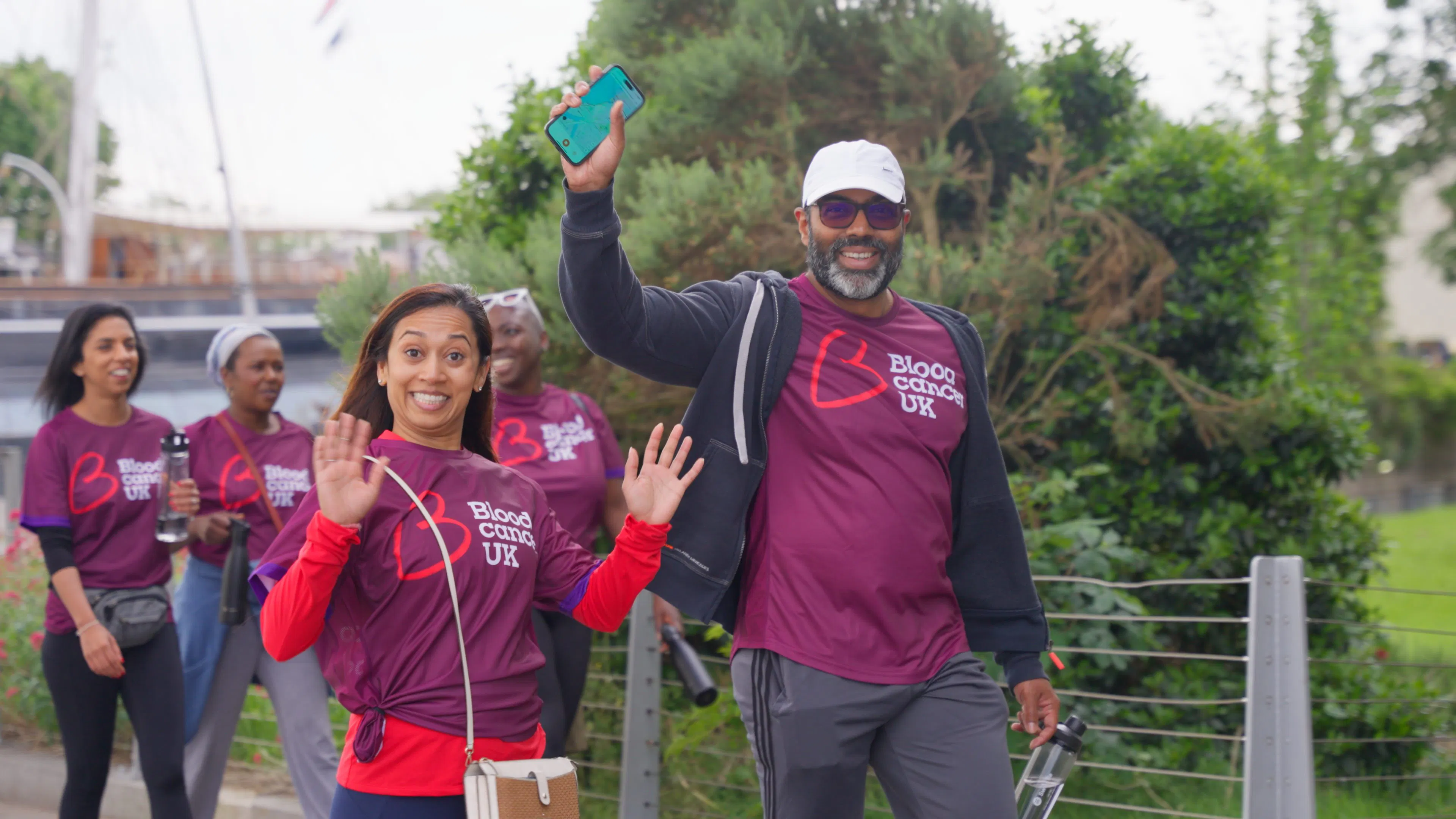 People wearing Blood Cancer UK t-shirts walk along a path, waving and holding water bottles during a charity event.