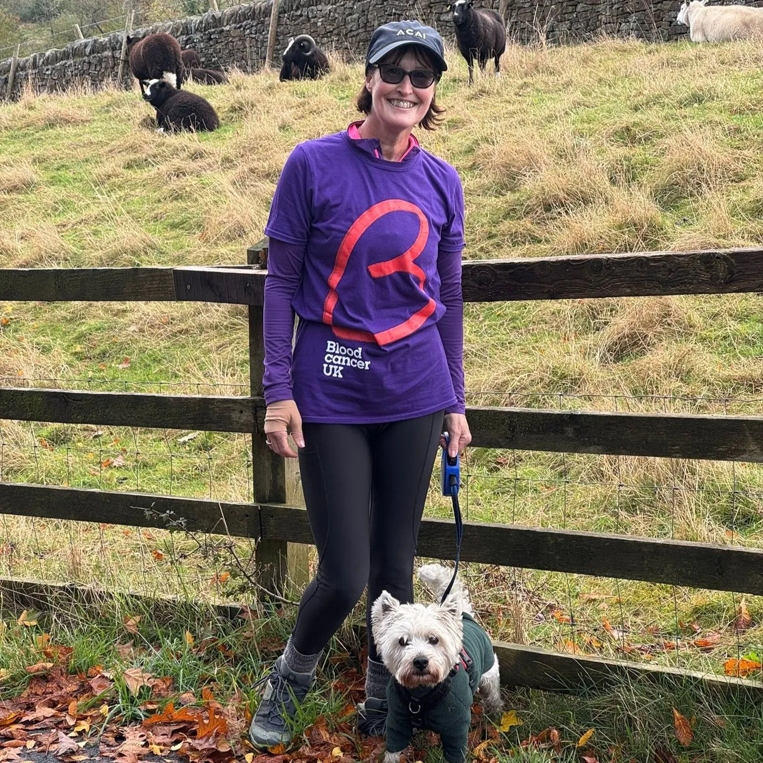 Denise walking with a small dog beside a countryside field, wearing a fundraising T-shirt.