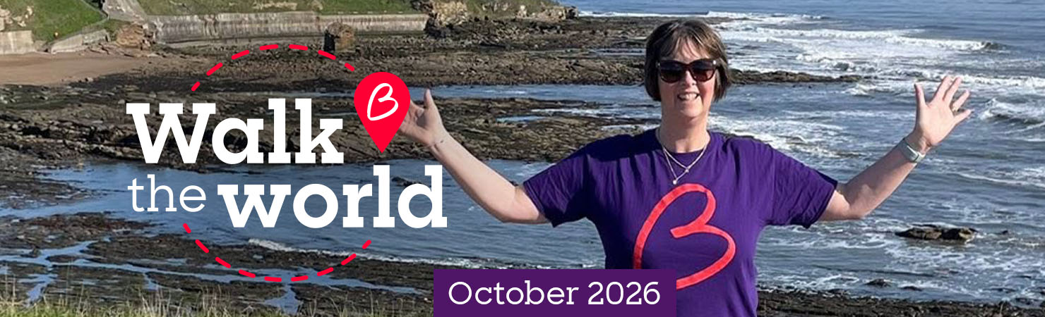 Person wearing a Blood Cancer UK t-shirt with arms outstretched, standing on a coastal cliff overlooking the sea for the Walk the World challenge, October 2026.