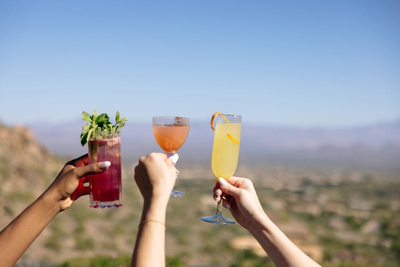 three people cheersing cocktails over desert landscape