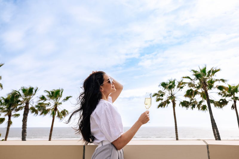 Woman standing on a balcony overlooking the sea with a glass of champagne