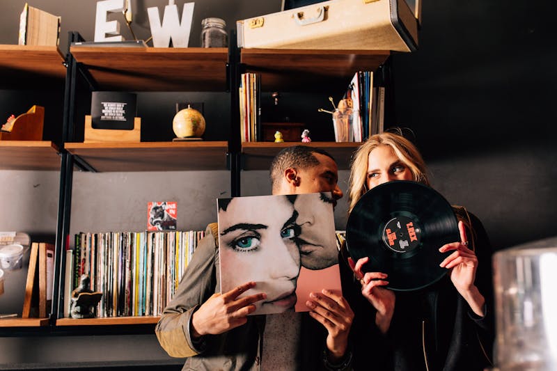 Man and a woman holding records in front of their faces while having a secret conversation behind them