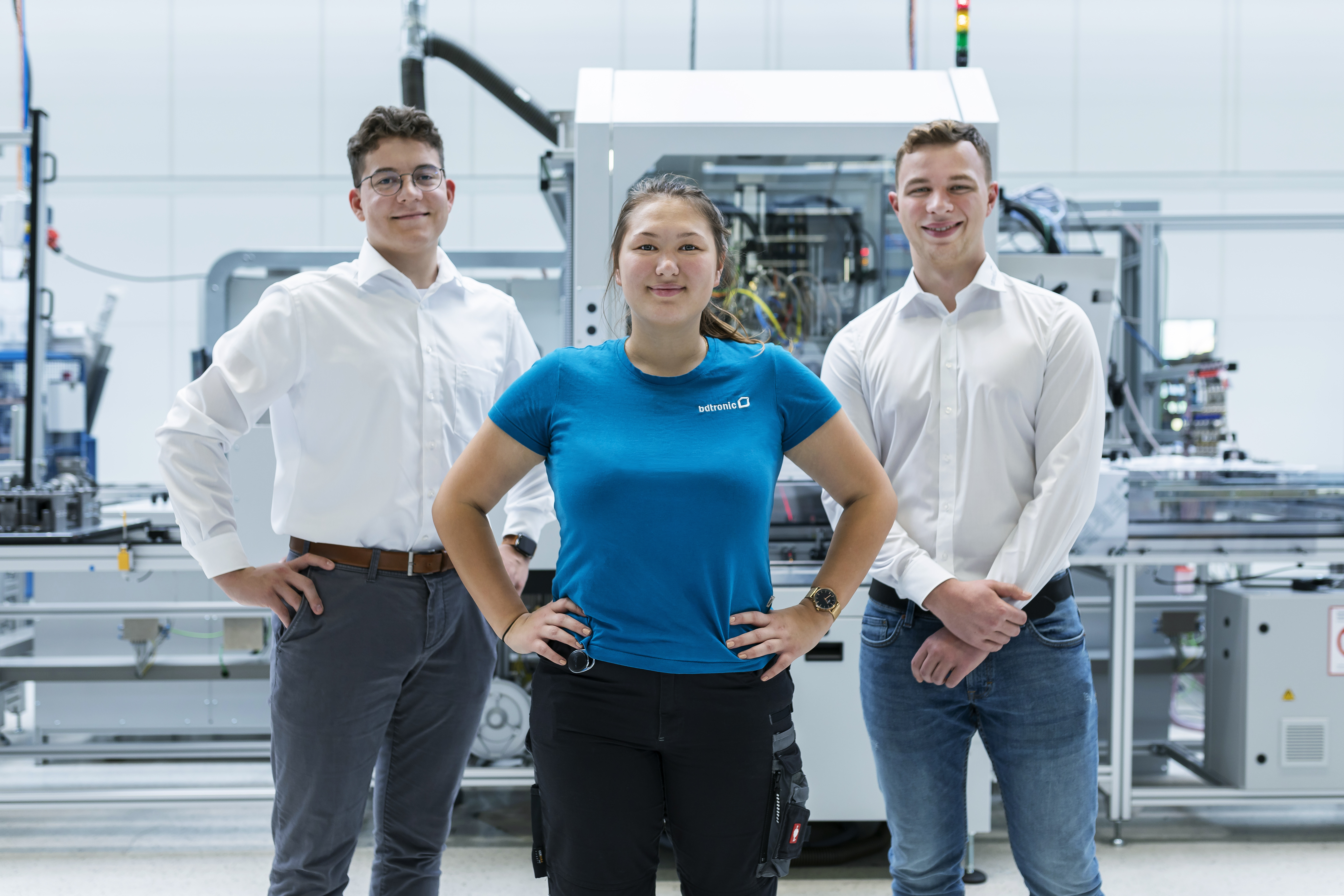 Three people stand in front of a machine with their hands on their hips