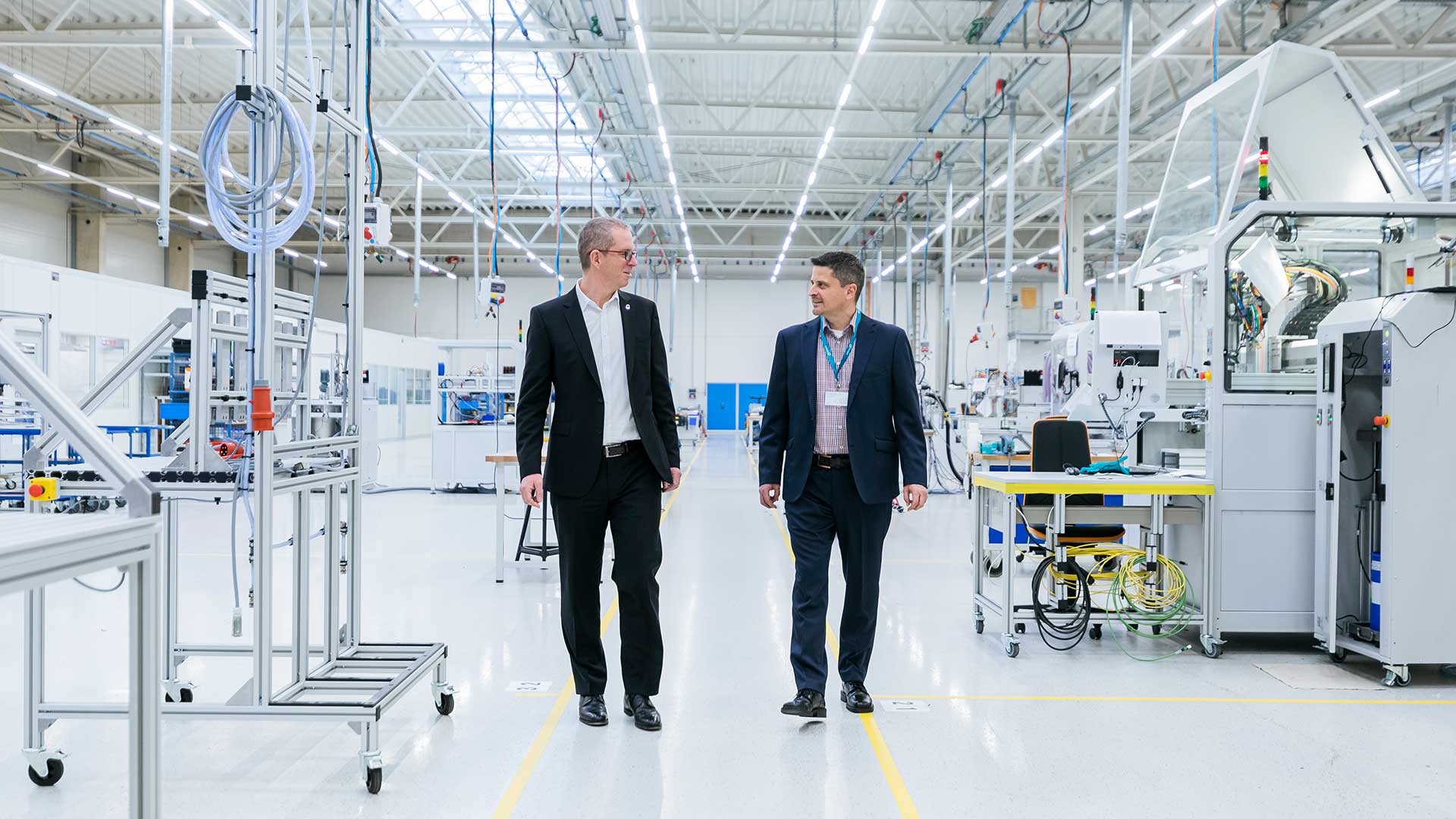 two people talk while walking through a production hall