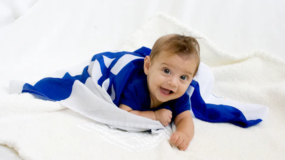 De vrolijke kleine Benzi ligt op zijn buik op de grond, gewikkeld in een Israëlische vlag.