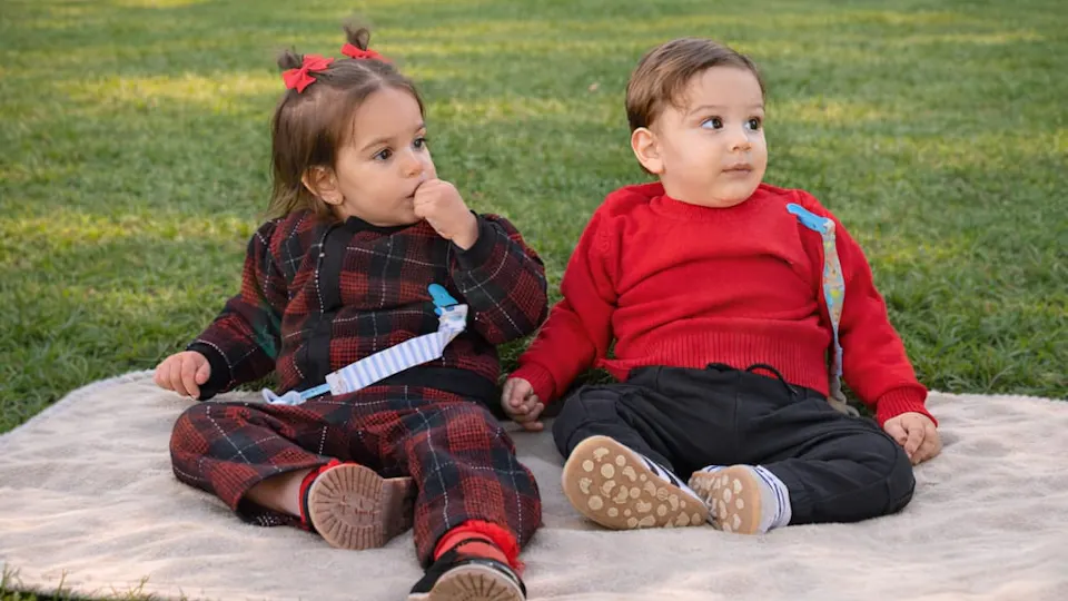 Toddler girl and boy sitting on a blanket on the grass