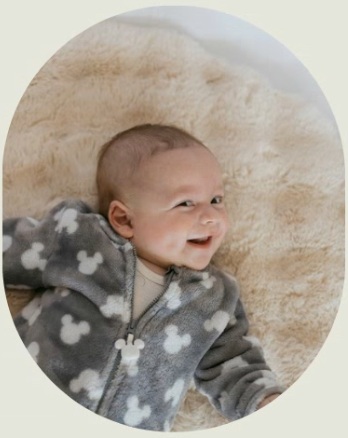 Sagie in a gray fleece jacket laying on the floor and side smiling to the camera