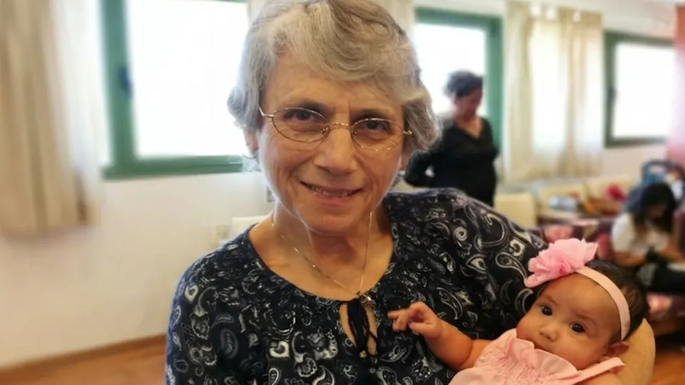 Sharon bij ons op kantoor, enkele jaren geleden, met een in het roze gekleed babymeisje op de arm.