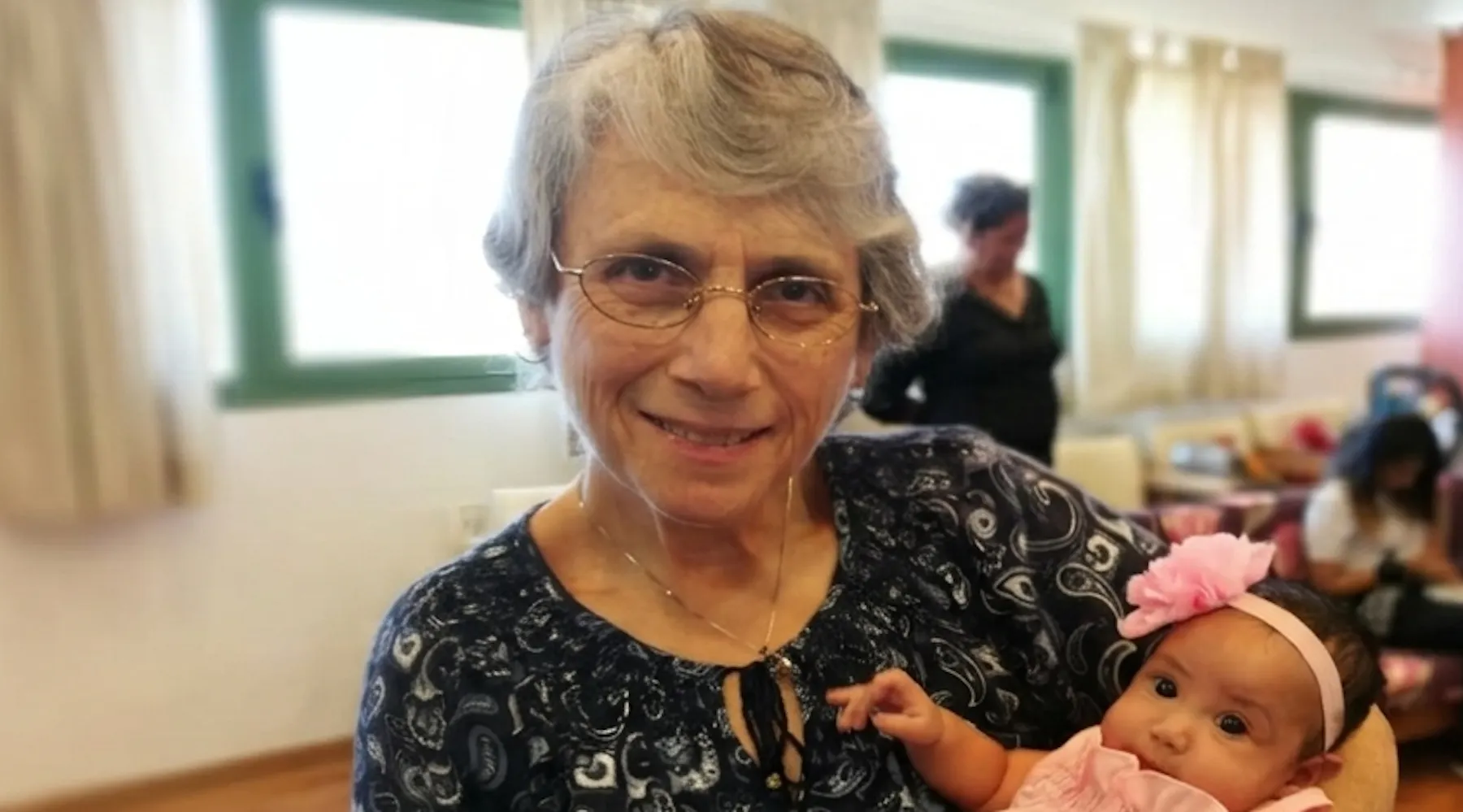 Sharon bij ons op kantoor, enkele jaren geleden, met een in het roze gekleed babymeisje op de arm.