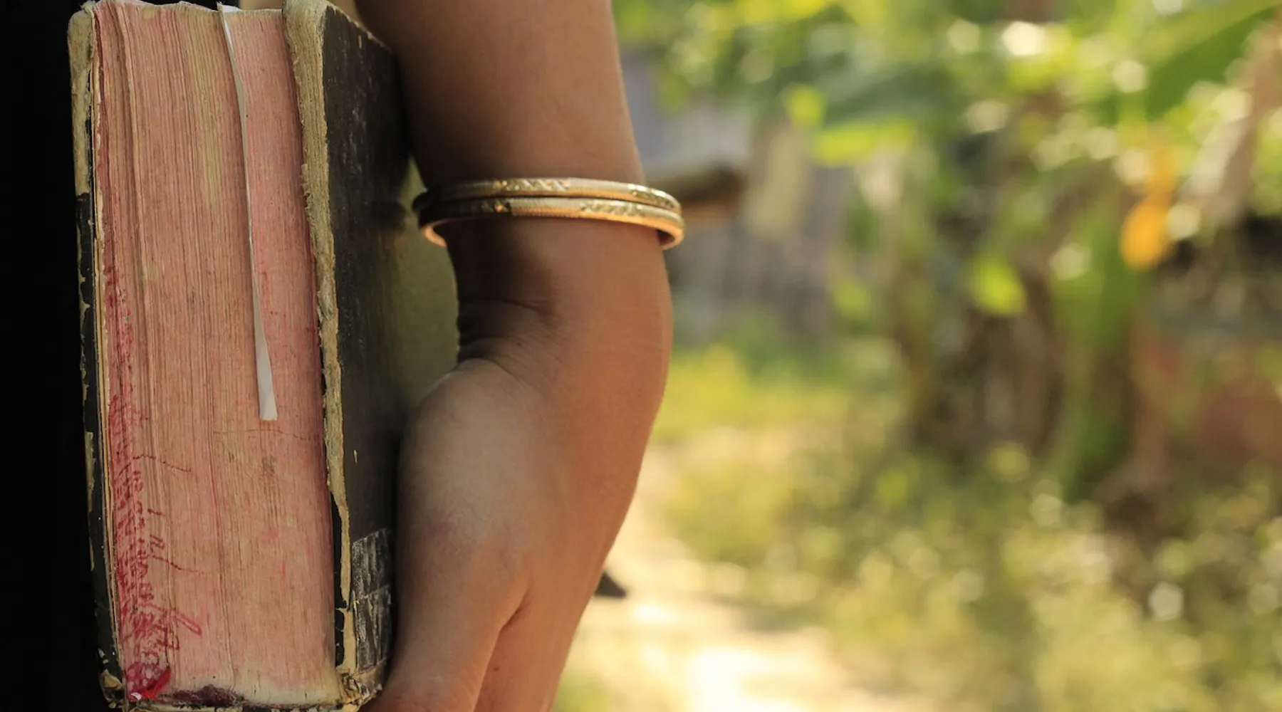 Vrouwenhand met een gouden armband die een oude bijbel vasthoudt.