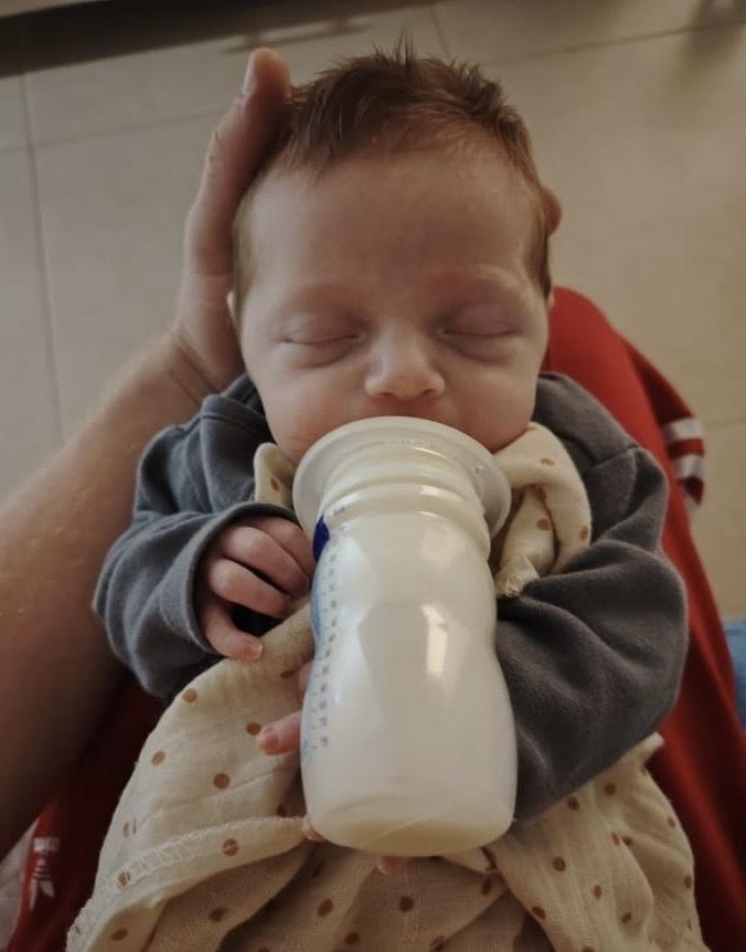 1 month old baby boy drinking milk from a bottle with closed eyes