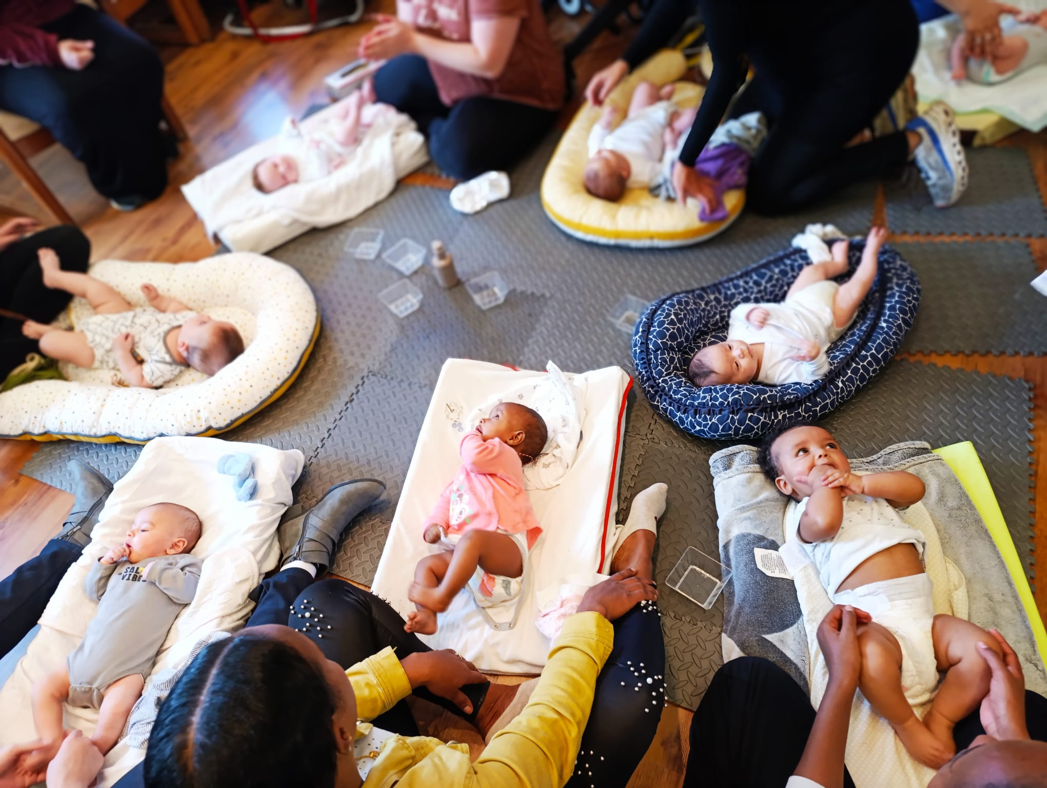 babies on blankets in a circle on the floor while their mothers gently massage them 