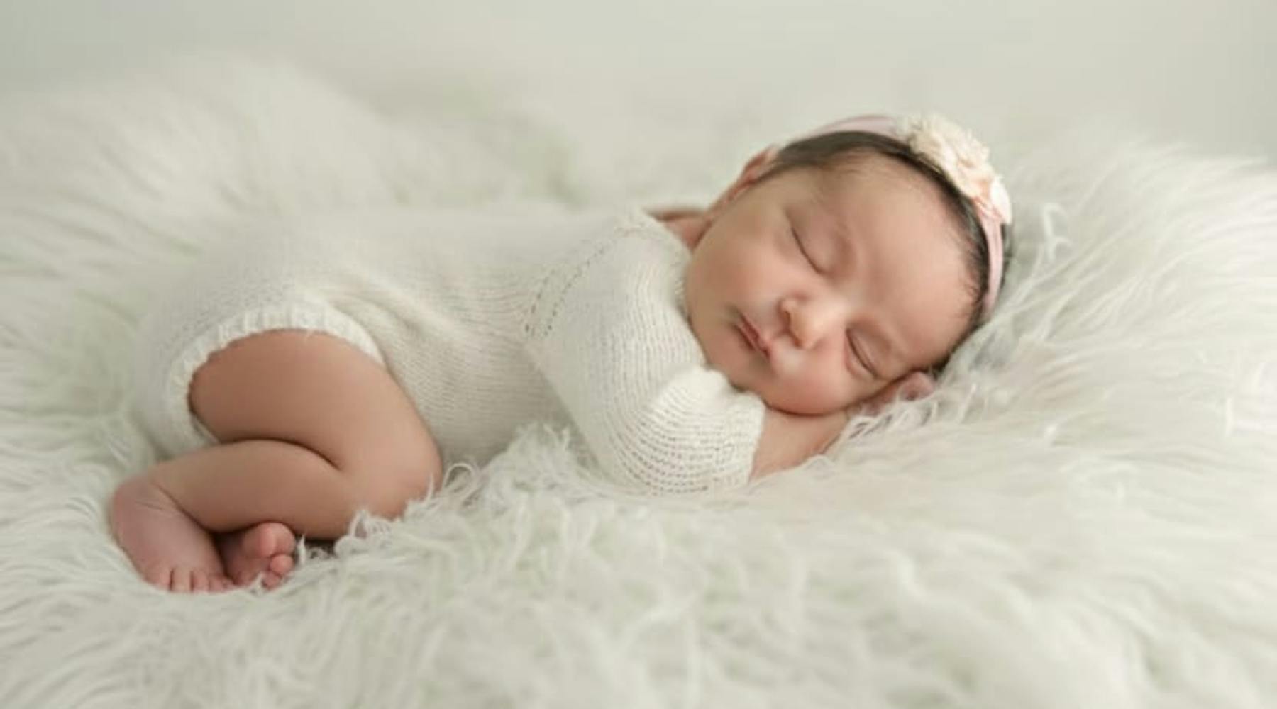 baby Penina in a white onsie on a white fleece and with a headband