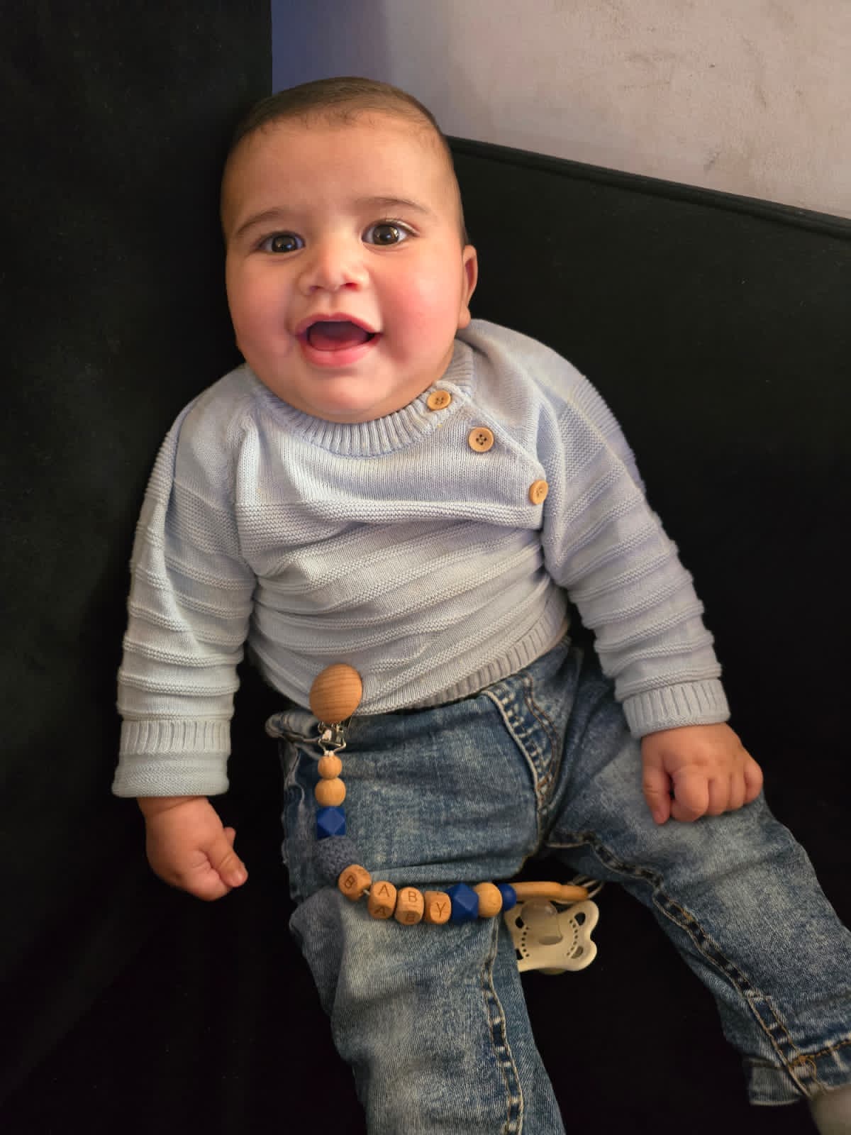 Noam met een brede glimlach in een blauwe raglan trui met knoopjes.