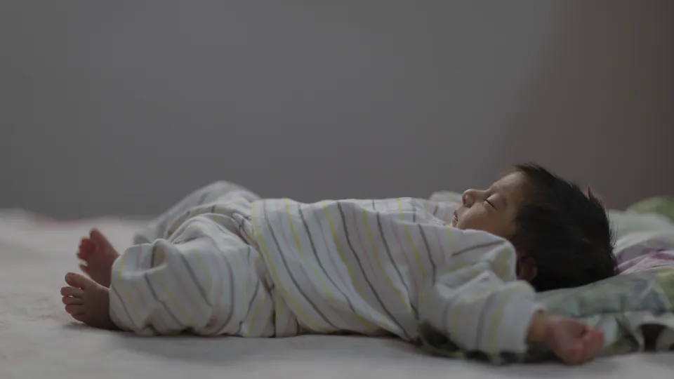 De baby slaapt op zijn rug met zijn armen omhoog naast zijn hoofd.