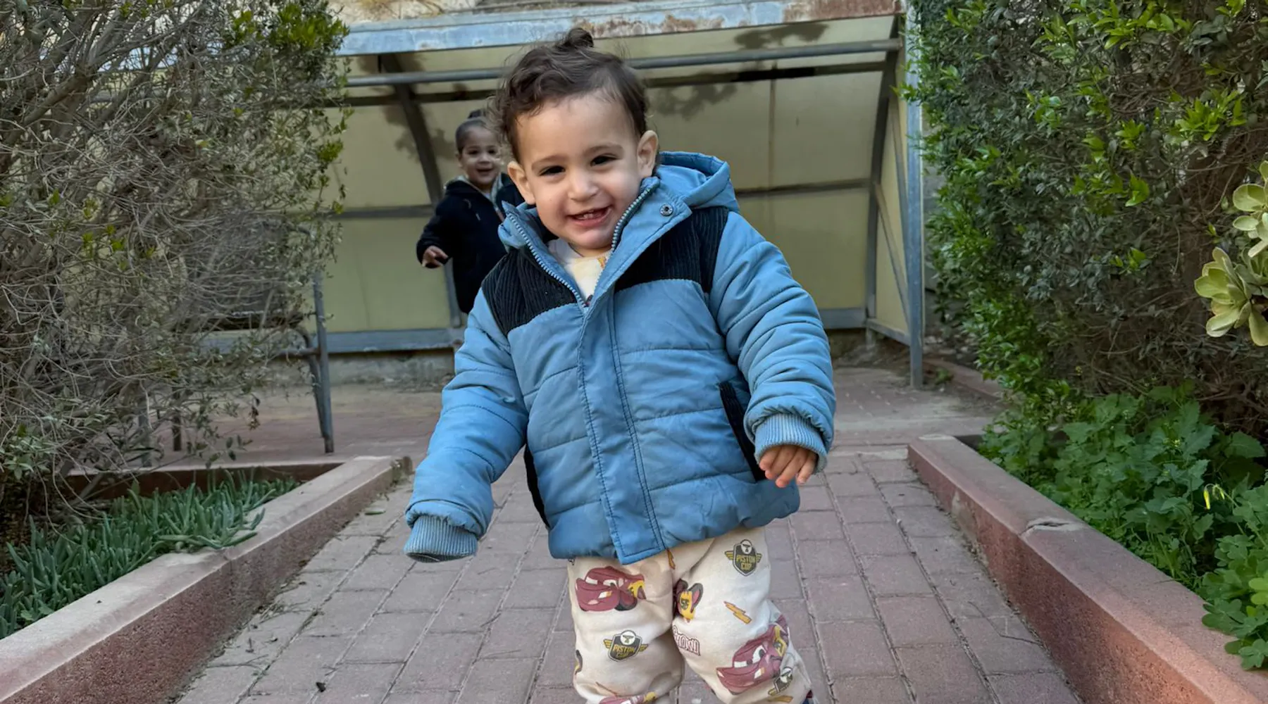 a boy in a blue jacket is walking down a path