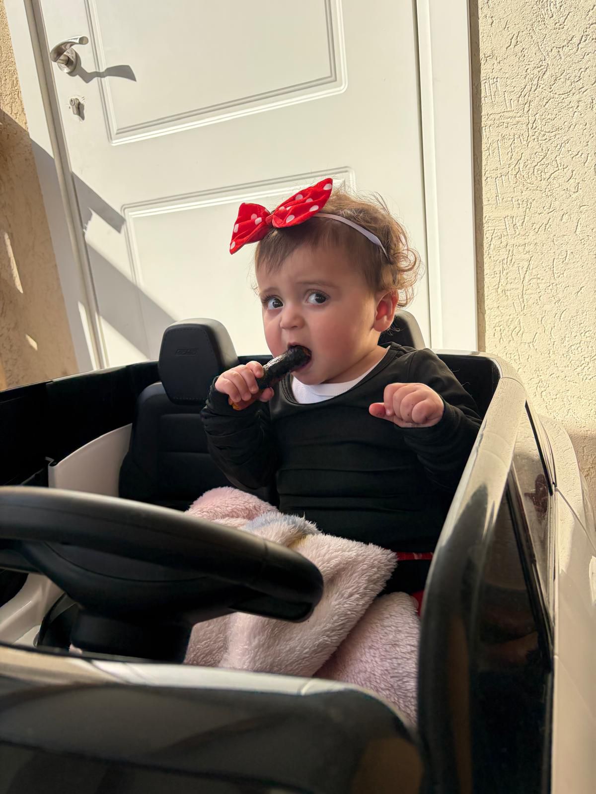 Baby elior with a red headband  and black shirt eating a cucumber