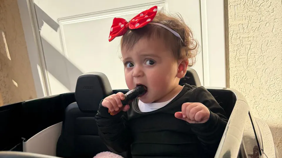 Baby elior with a red headband and black shirt eating a cucumber