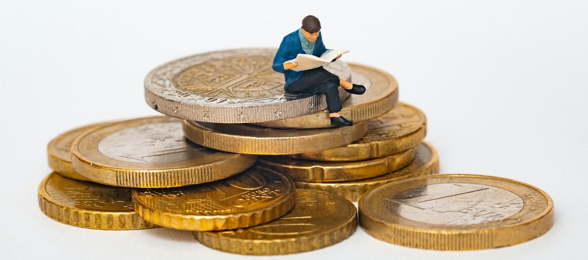 A figure of a man doing research, sitting on a pile of coins. Research on how to choose a lender when purchasing an investment property.