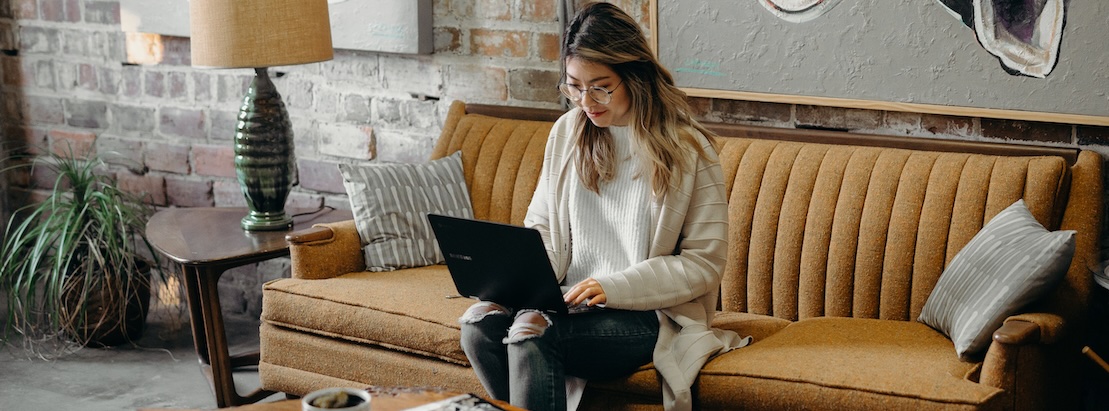 A young woman sits on a sofa with her laptop, searching for a rental home