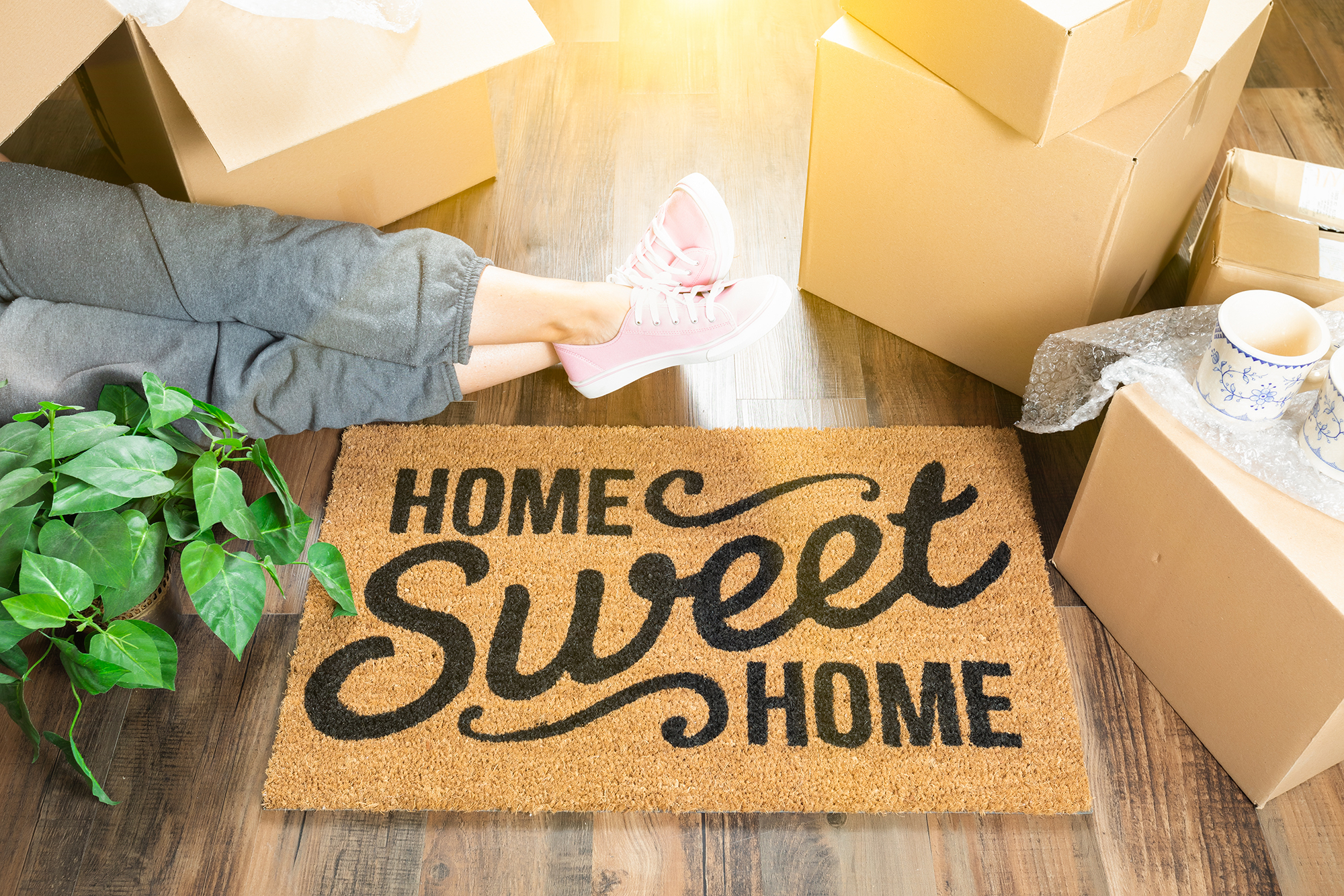 Welcome mat that says "home sweet home", showing a person relaxing among moving boxes and making themselves at home