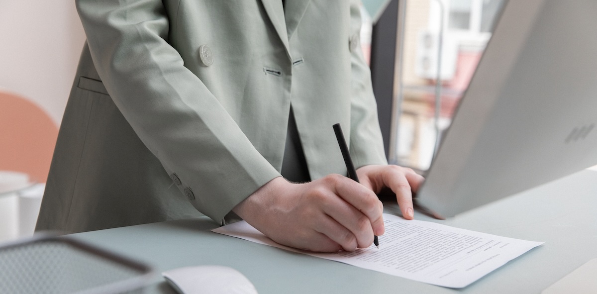 A woman in a sage-green jacket reviews a lease agreement for her rental home at a computer desk, her face is not visible