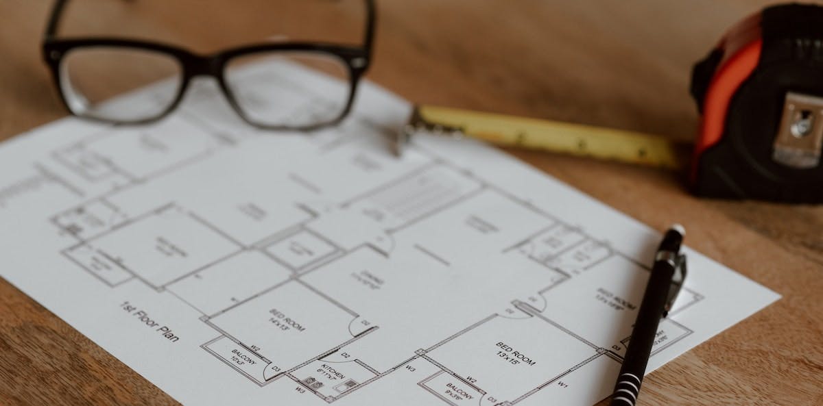 An image of house plans with a measuring tape, pencil and glasses. Learn the guidelines that stipulate how to calculate the square footage of your rental home.