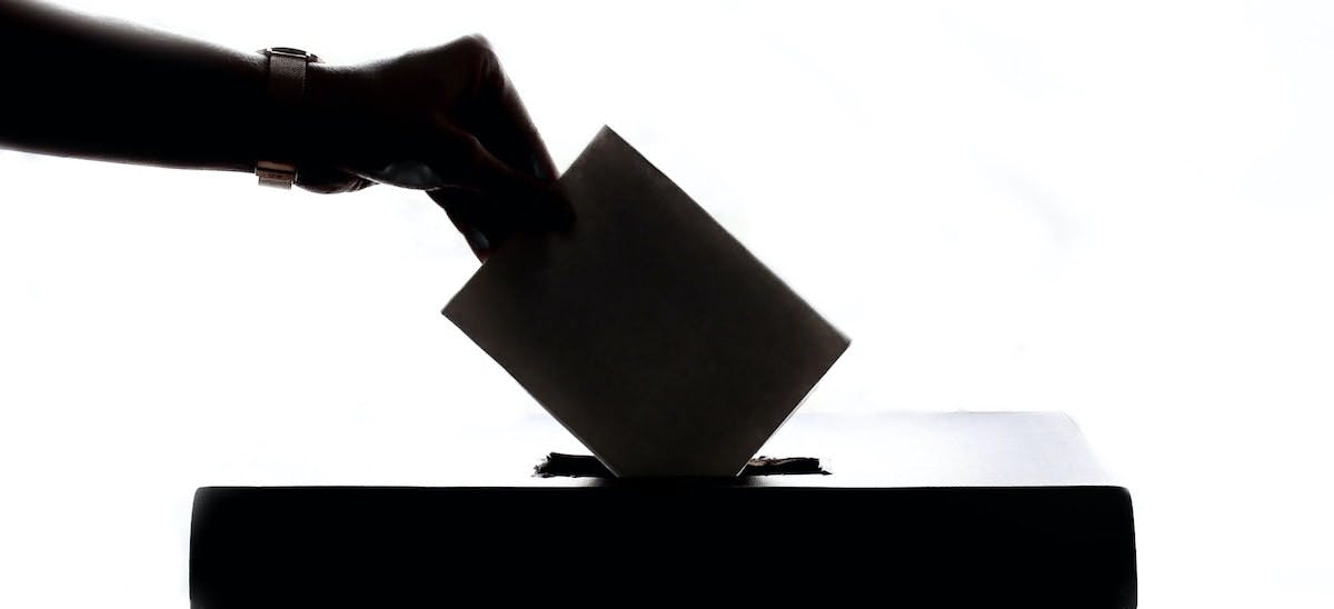 A silhouette of a voter placing their voting card in a ballot box. Learn more about the ballot initiatives that passed in November 2022 and how they could impact real estate investors and rental home owners. 