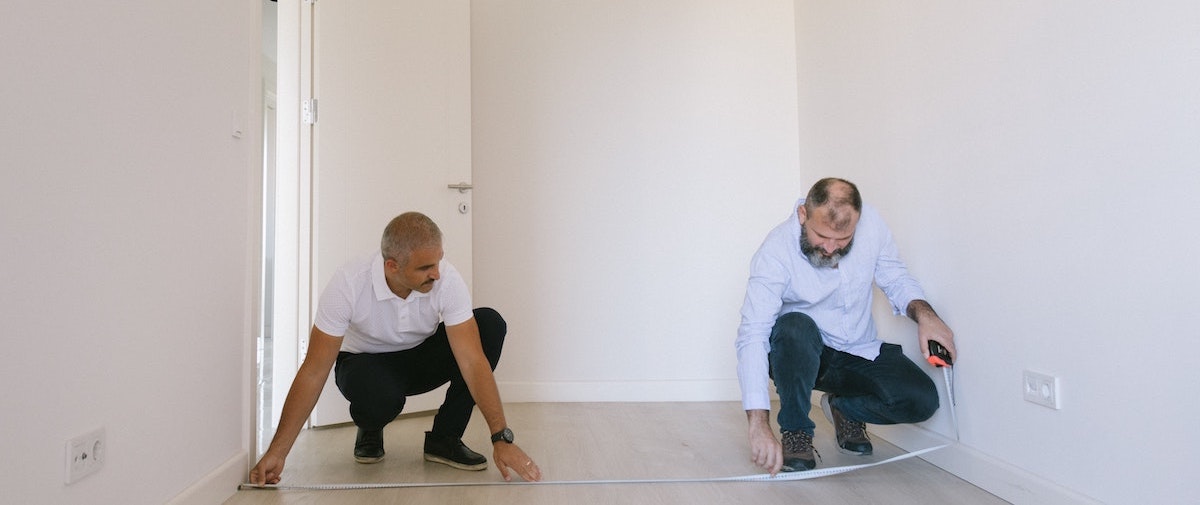 Two men measure the dimensions of a vacant rental home