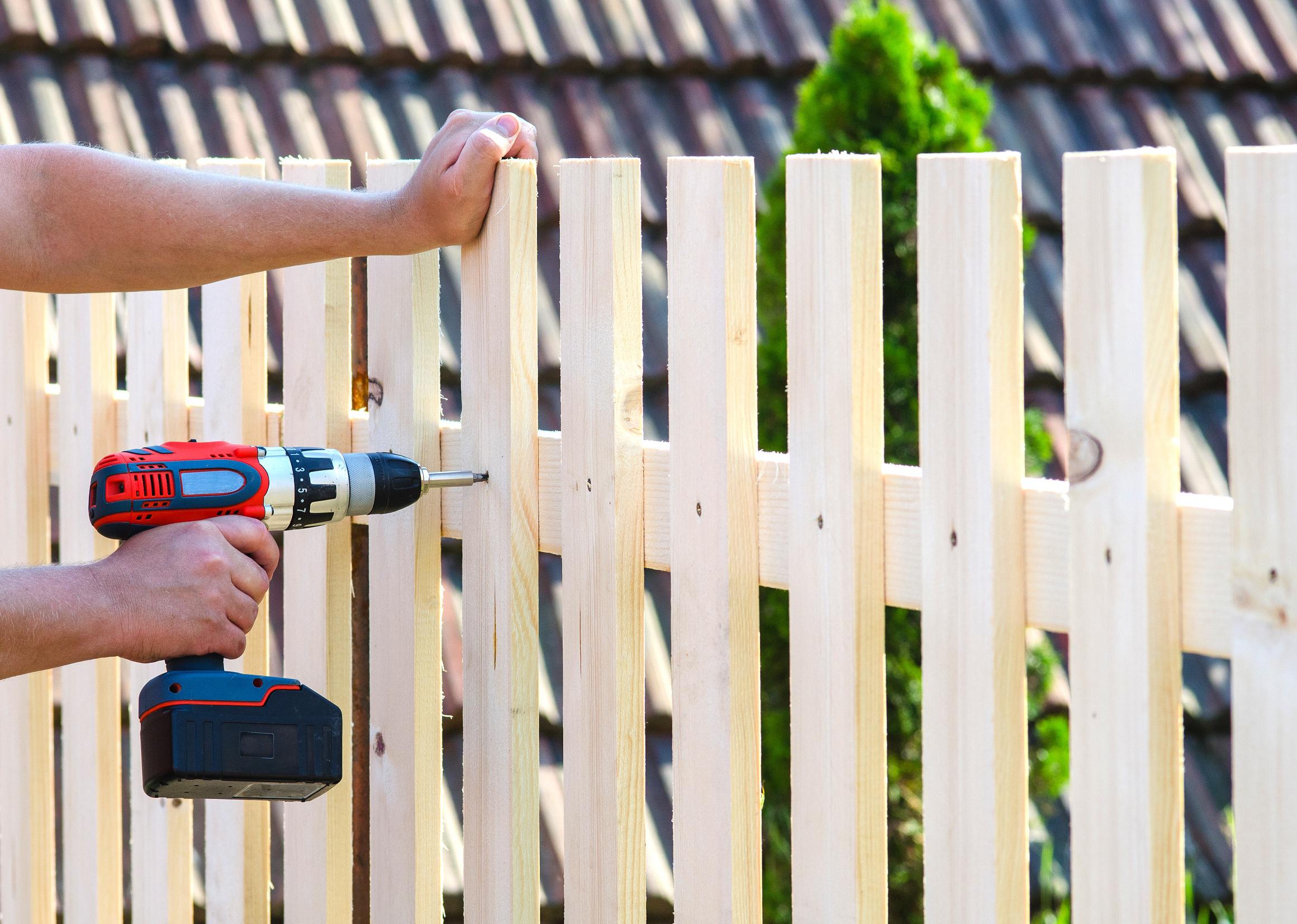 A hand drilling posts on a brand new fence