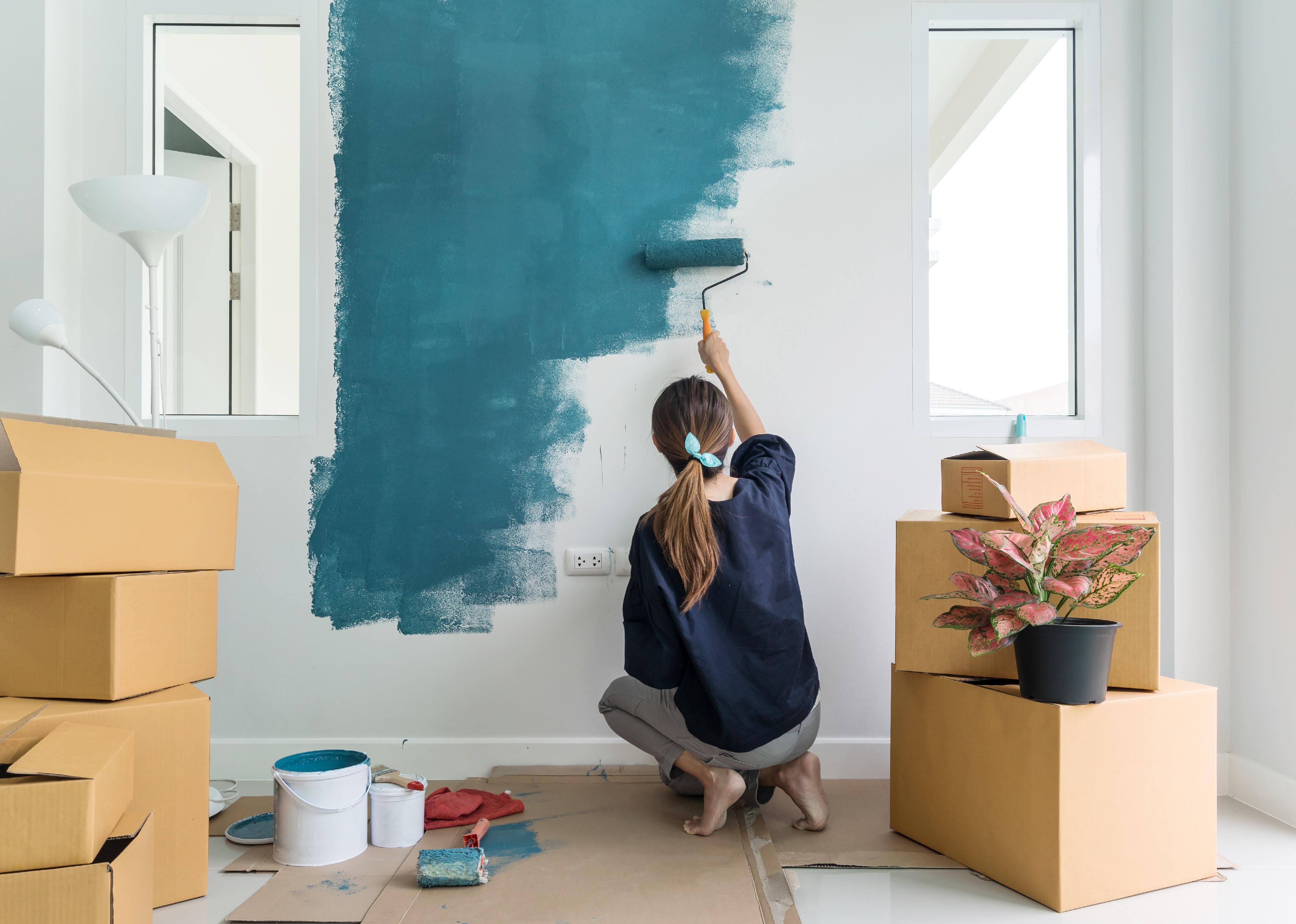 An image of a young woman renovating her home by painting a wall with teal-green paint color