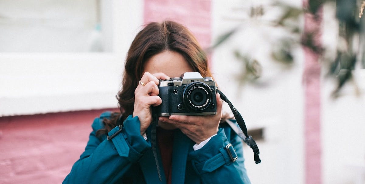 A young woman holds a camera outside a home, capturing real estate photography to market and list a rental home