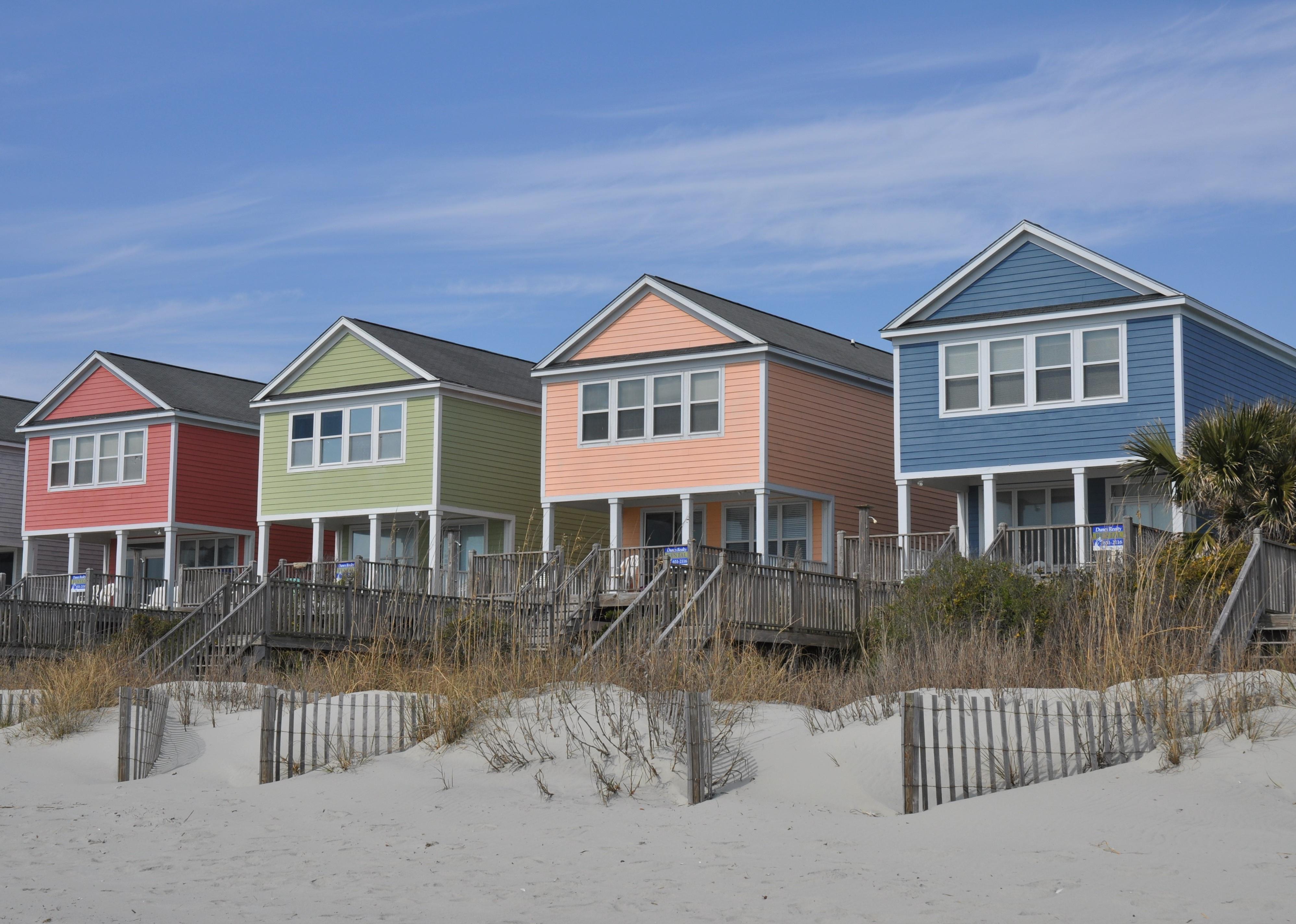 An image of four colorful beach homes in red, green, pink and blue with white windows