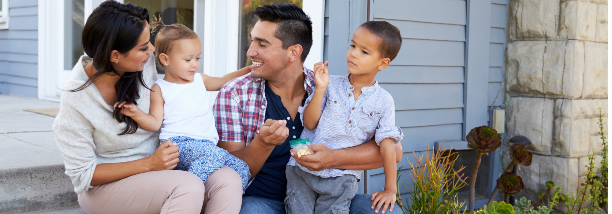 A young and diverse family in California, sitting on the porch steps with two young children outside an ADU
