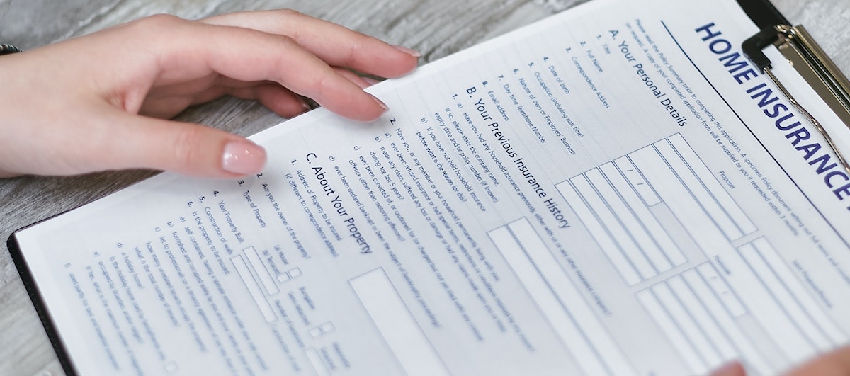 An image of a hand over a home insurance policy. Learn more about renters insurance and if you should require tenants to have a policy.