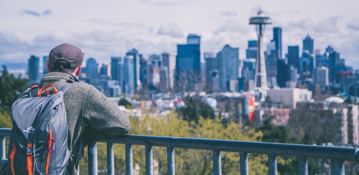 A man with a backpack is exploring Seattle's most walkable neighborhoods, standing at a lookout of the Space Needle and city