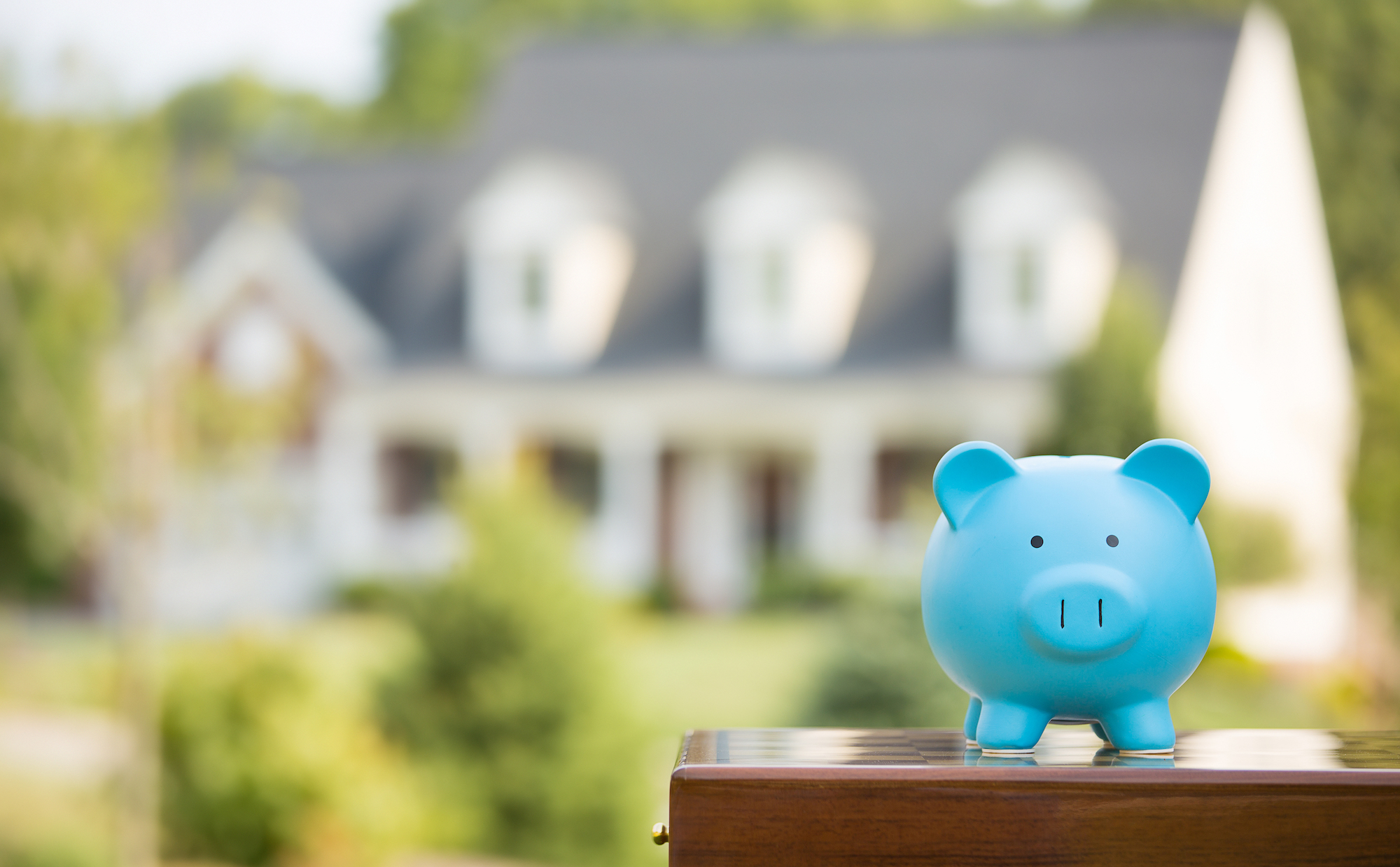 A blue piggybank sitting on a letterbox with a rental property in the background, depicting no loss of rental revenue