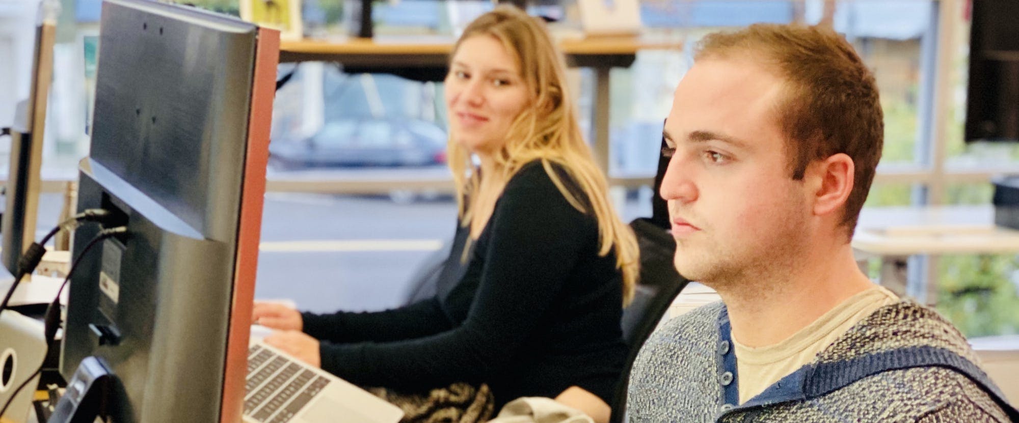 Two Belong employees pictured working in the office at their computers