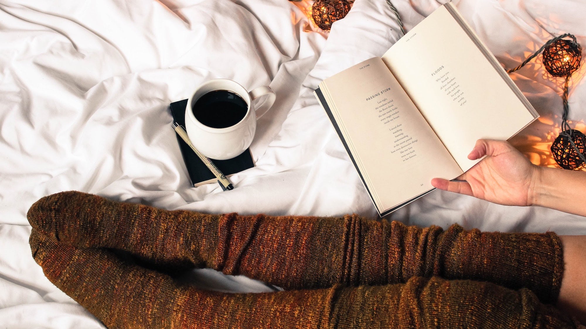 A pair of socks, poetry book and coffee laid out on a white bed spread