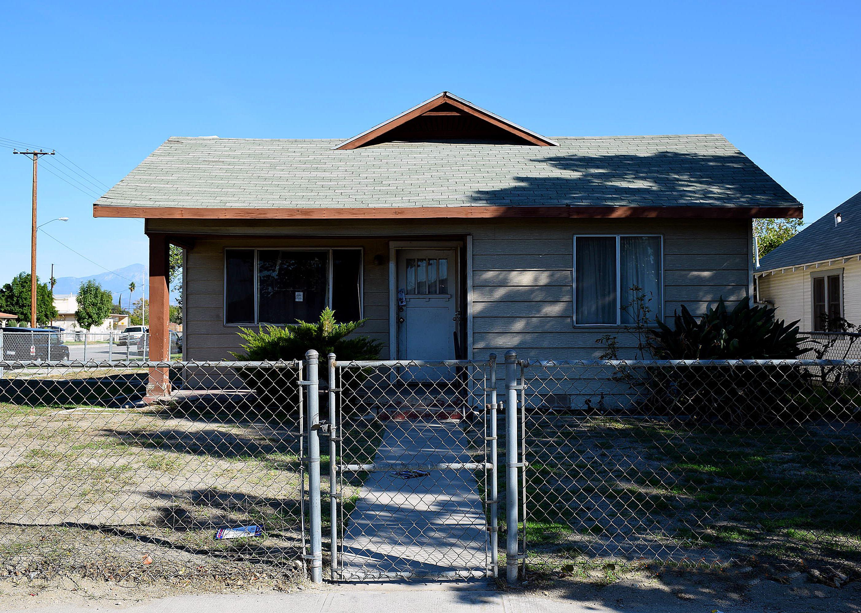 An old home with a grey chain link fence and bare front yard