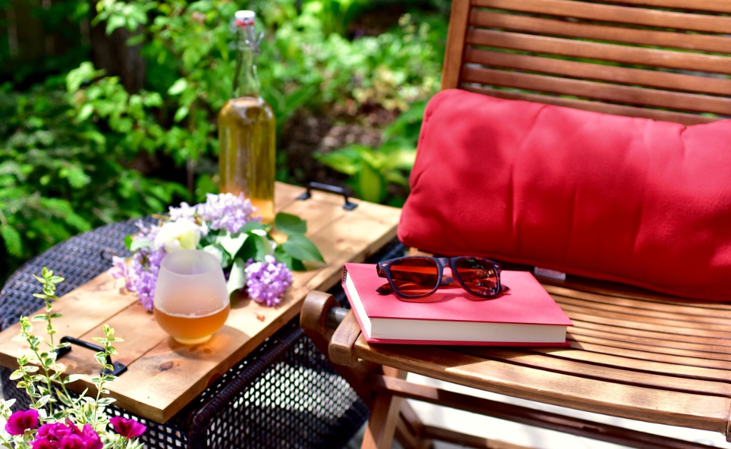 A comfortable outdoor space with a deck chair, book, floral arrangement and iced tea to enjoy
